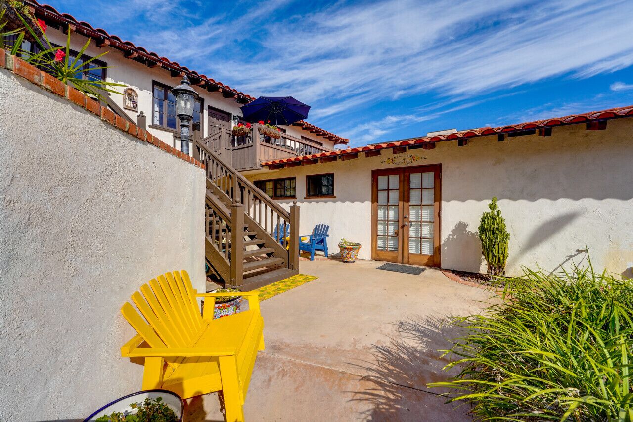 A courtyard with a yellow chair, a wooden staircase, and a building with a red-tiled roof.