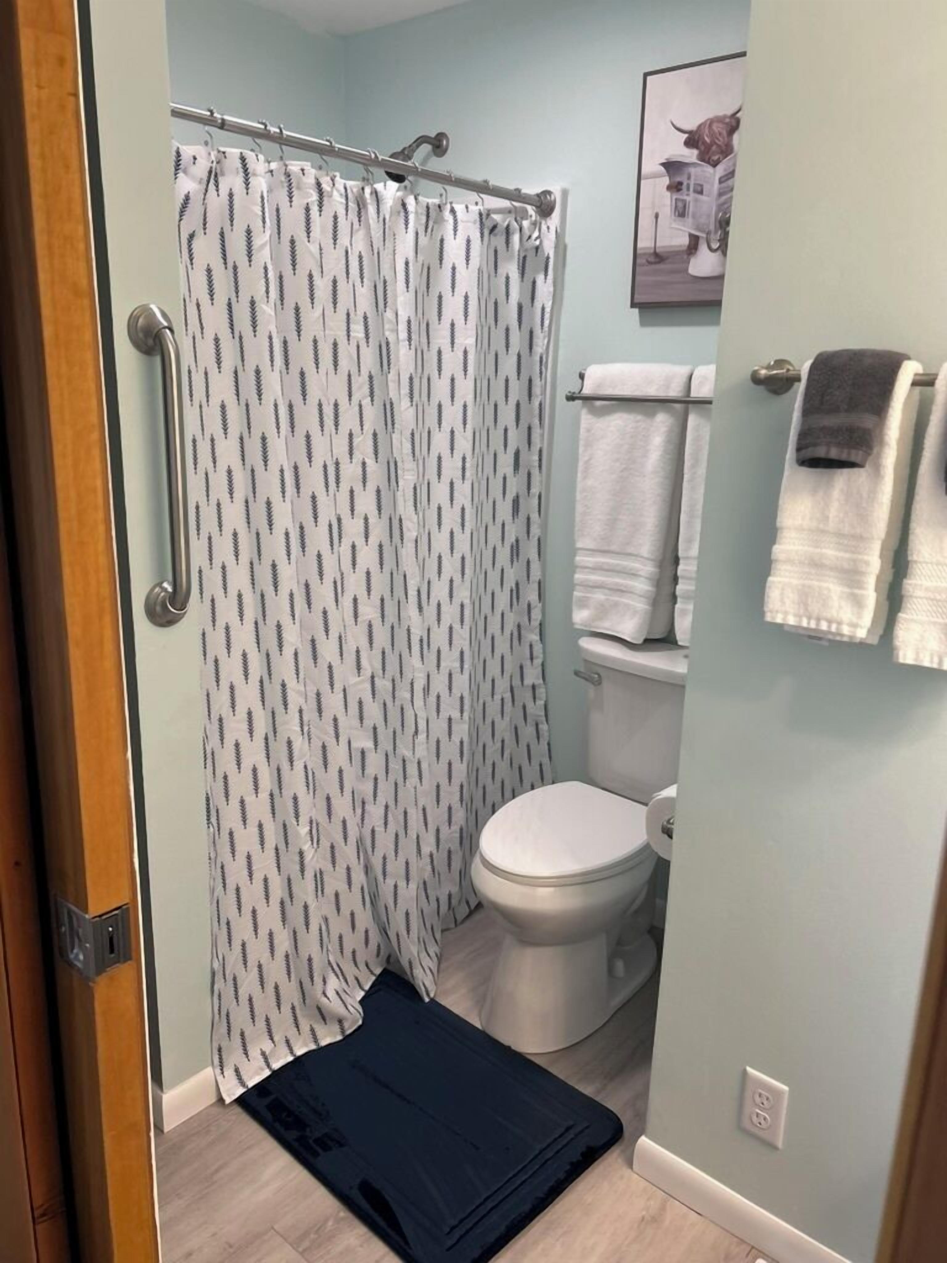 Une salle de bain avec un rideau de douche, des toilettes et un porte-serviettes avec des serviettes.