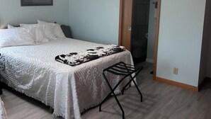 Ein Schlafzimmer mit einem Bett, einem Deckenventilator, einem gerahmten Bild an der Wand und einer Tür zu einem anderen Raum.