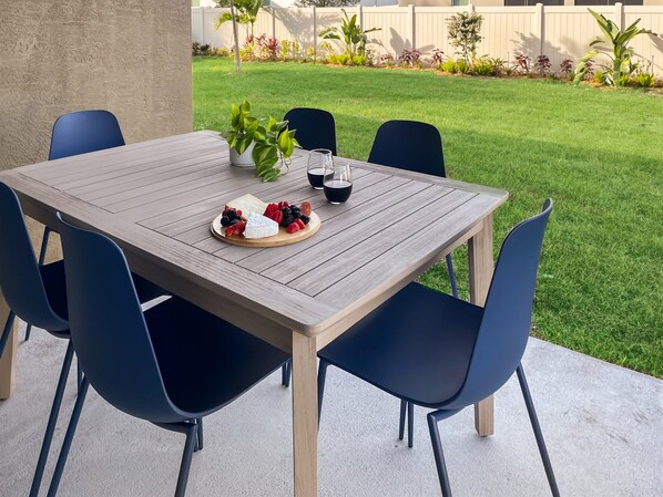 An outdoor patio with a wooden table set for a meal, surrounded by chairs.