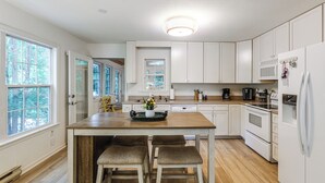 Una cocina con armarios blancos, una isla de madera con taburetes, un microondas y un refrigerador.