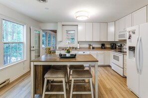 A kitchen with white cabinets, a wooden island with stools, a microwave, and a refrigerator. - 2 Mi to Bethany Beach! Family Home w/ Deck (Frankford)