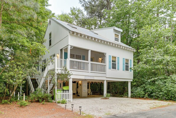 A two-story building with a porch, a staircase, and a sign that reads 'BEACH HOUSE.'