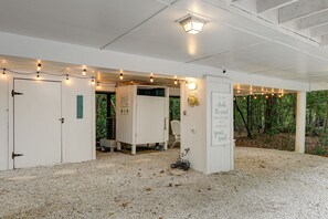 A building with white walls, a gravel floor, and string lights. There are doors, a bench, and a sign with text.