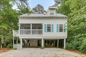A two-story beach house with a balcony, a covered porch, and a gravel driveway.