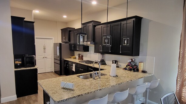A modern kitchen with dark cabinets, a granite countertop, and a central island with bar stools. - Unique and Stylish Modern House  (Midlothian)