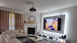 A modern living room with a large flat-screen TV, a fireplace, and a sectional sofa. - Unique and Stylish Modern House  (Midlothian)