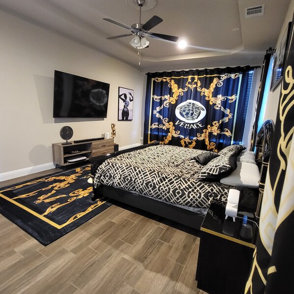 A modern bedroom with a bed, a ceiling fan, a flat-screen TV, and a decorative curtain.