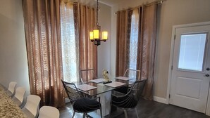 A dining area with a glass table and chairs, a chandelier, and a door with a window. - Unique and Stylish Modern House  (Midlothian)