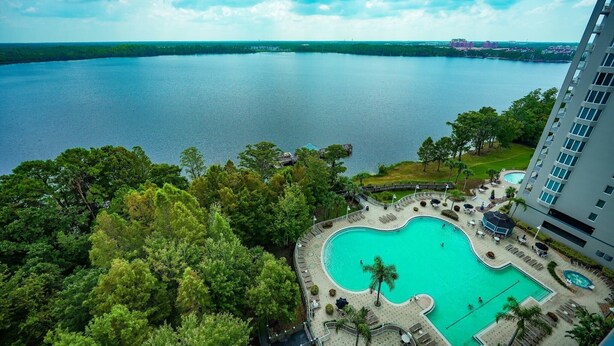 A hotel with a large pool surrounded by lush greenery and a view of a large body of water.