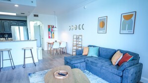 A modern living room with a blue sofa, a coffee table, and a dining area with chairs and a table.