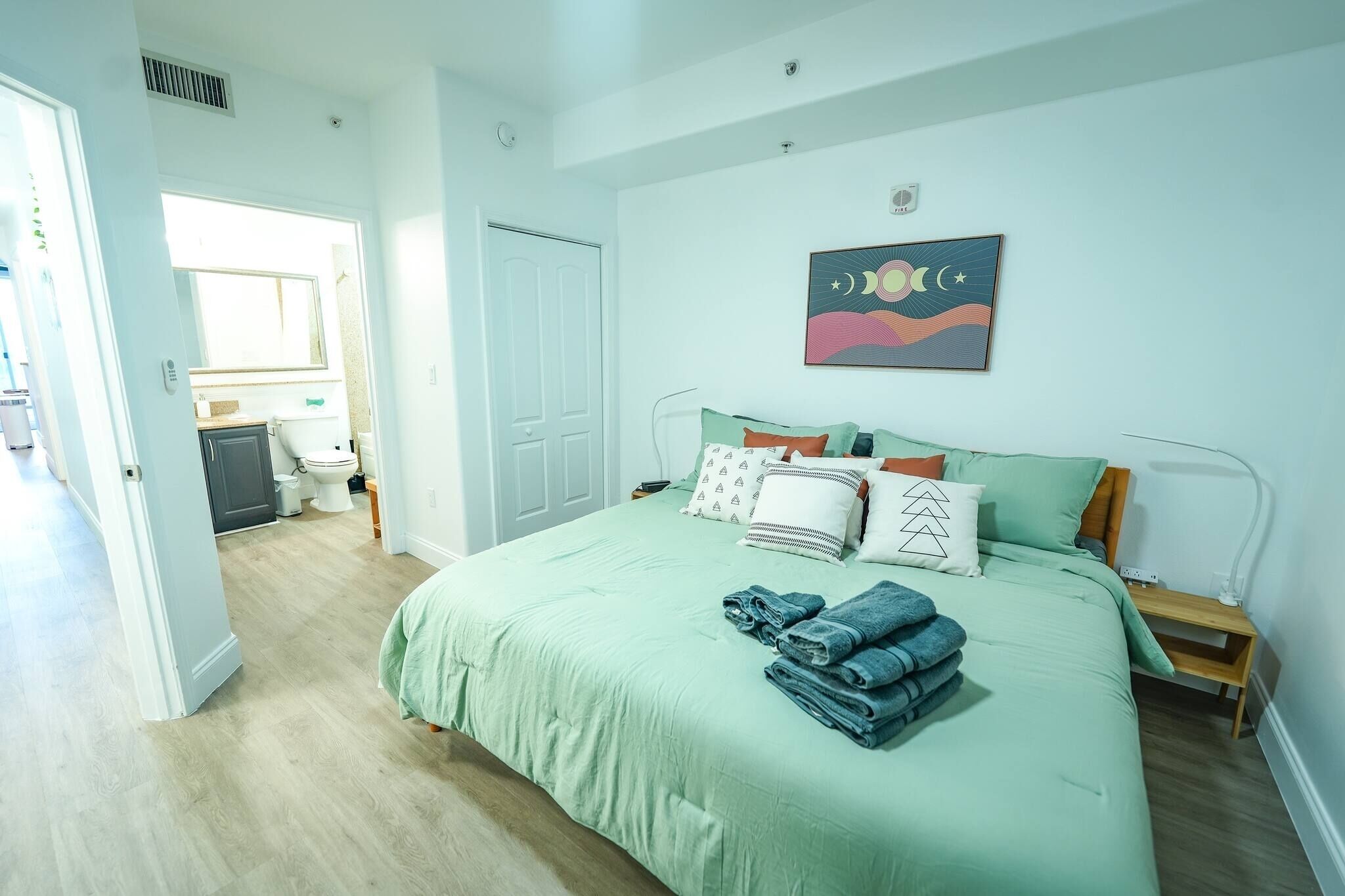 A bedroom with a bed, pillows, a bedside table, and a wall art piece.