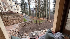 Un patio con dos sillas y una mesa, un muro de piedra y vistas a un edificio y árboles.