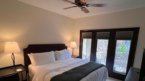 Habitación de hotel con cama, dos mesitas de noche, lámparas, ventilador de techo y un ventanal con persianas.