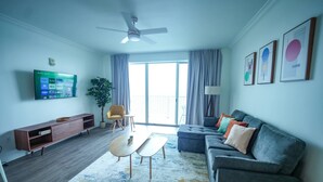 Una sala de estar moderna con un televisor de pantalla plana, un ventilador de techo, un sofá, una mesa de centro y un ventanal con cortinas.