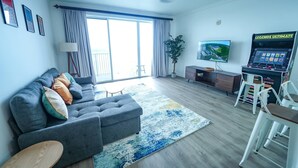 Una sala de estar con sofá, mesa de centro, televisor, ventilador de techo y consola de videojuegos.