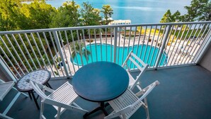 A balcony with a view of a lake, a pool, and white outdoor furniture.