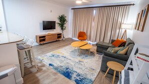 A modern living room with a sofa, coffee table, TV, and a dining area with chairs and a wooden cabinet.
