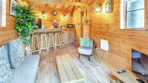 Un intérieur de chalet chaleureux avec un plafond en bois, un coin repas avec des tabourets, un bar, un coin salon avec un canapé et un téléviseur.