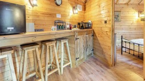 L’intérieur d’un chalet en bois comprend un coin cuisine équipé d’un réfrigérateur, d’un four à micro-ondes, d’une bouilloire et de tabourets de bar.