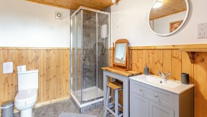 Une salle de bain avec un plafond en bois, une cabine de douche en verre, des toilettes, un lavabo avec un miroir et un tabouret en bois.