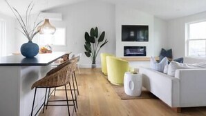 Ein modernes Wohnzimmer mit einem weißen Sofa, einem gelben Sessel, einer Essecke mit einem Barhocker und einer großen Pflanze.