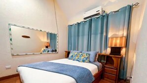 A bedroom with a bed, a nightstand, a lamp, a mirror, and an air conditioning unit.