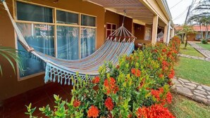 A house with a hammock, large windows, and a garden with colorful flowers.