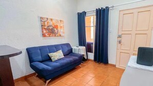 A room with a blue sofa, a small round table, a painting on the wall, a window with curtains, and a door.