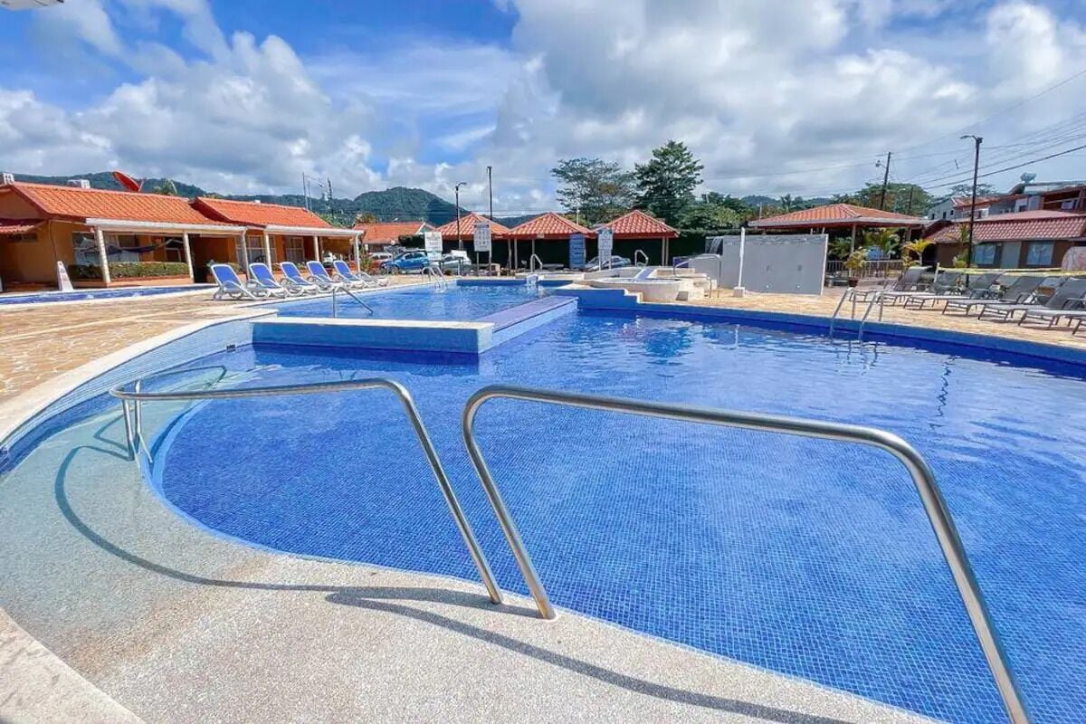 A swimming pool with a blue tiled deck, a metal pool ladder, and lounge chairs.