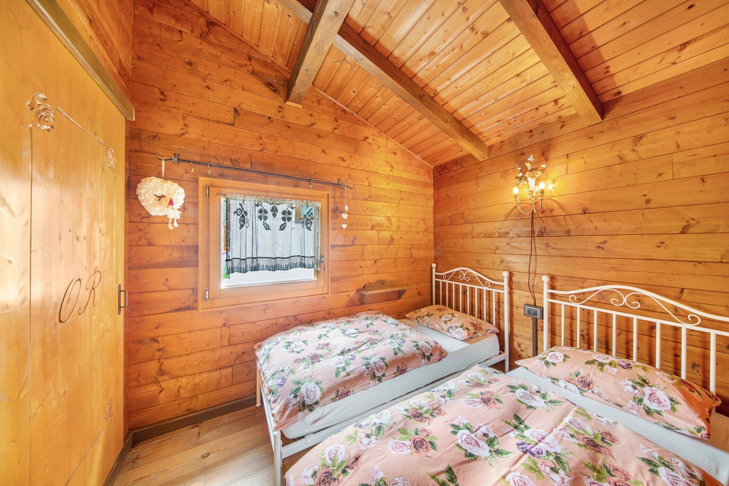 Ein Schlafzimmer einer Holzhütte mit zwei Betten, einem Fenster mit Vorhang und einer Chandelier.