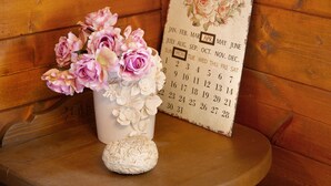 A wooden wall with a calendar and a vase of flowers.