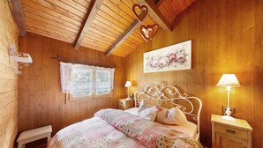 Een kamer met houten vloeren, een bed, twee bedlampen, een bankje en een raam met gordijn.