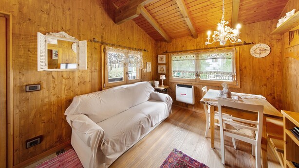 Een houten interieur met een bank, eettafel, stoelen, een kroonluchter en een klok aan de muur.