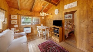 Een houten blokhut van binnen, met een bank, een eettafel, stoelen, een televisie en een bed.