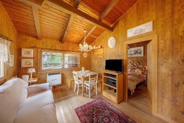 A wooden cabin interior with a sofa, dining table, chairs, a TV, and a bed.