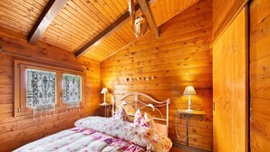 Een slaapkamer in een houten chalet, met een bed, twee bedlampjes en een raam met decoratieve gordijnen.