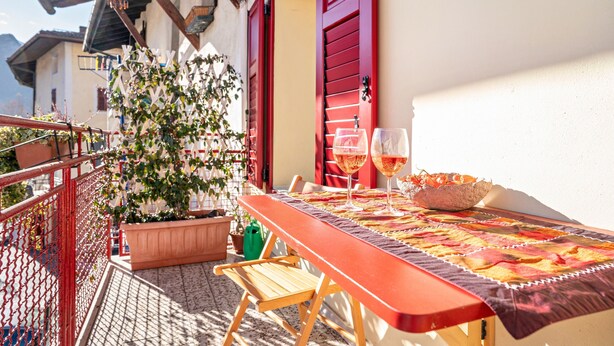 Een balkon met een tafel voor twee personen, een bloempot en een rode deur.