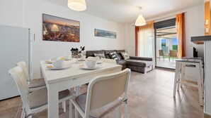 Un salon moderne avec un coin repas, des meubles blancs et des œuvres d’art accrochées aux murs.