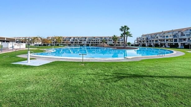 Une piscine entourée d’une pelouse bien entretenue, avec un immeuble à plusieurs étages en arrière-plan.