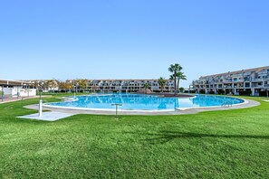 Une piscine entourée d’une pelouse bien entretenue, avec un immeuble à plusieurs étages en arrière-plan.
