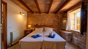 A room with two beds, a stone wall, a wooden ceiling, a window with a view, and a nightstand with a lamp. - Country House 'Cugulutx' with Private Pool, Private Terrace and Wi-Fi (Llucmajor)
