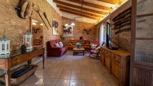 A rustic living room with stone walls, wooden beams, a red sofa, a wooden coffee table, and a television. - Country House 'Cugulutx' with Private Pool, Private Terrace and Wi-Fi (Llucmajor)