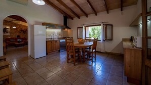 A kitchen with wooden beams, a refrigerator, a dining table with chairs, and a window with curtains. - Country House 'Cugulutx' with Private Pool, Private Terrace and Wi-Fi (Llucmajor)