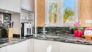 A kitchen with a coffee machine, a sink, and a window with a view of palm trees. - Villa 'Casasilma' with Sea View, Wi-Fi and Air Conditioning (POBLE NOU DE BENITATXELL)