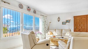 A living room with a sofa, armchair, and a coffee table. There are decorative plates on the wall and a view of the outside. - Villa 'Casasilma' with Sea View, Wi-Fi and Air Conditioning (POBLE NOU DE BENITATXELL)