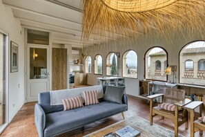 A spacious living area with a sofa, chairs, a dining table, and a large window with a view. - Apartment 'El Pedró Rural' with Mountain View, Wi-Fi and Air Conditioning (Ventalló)
