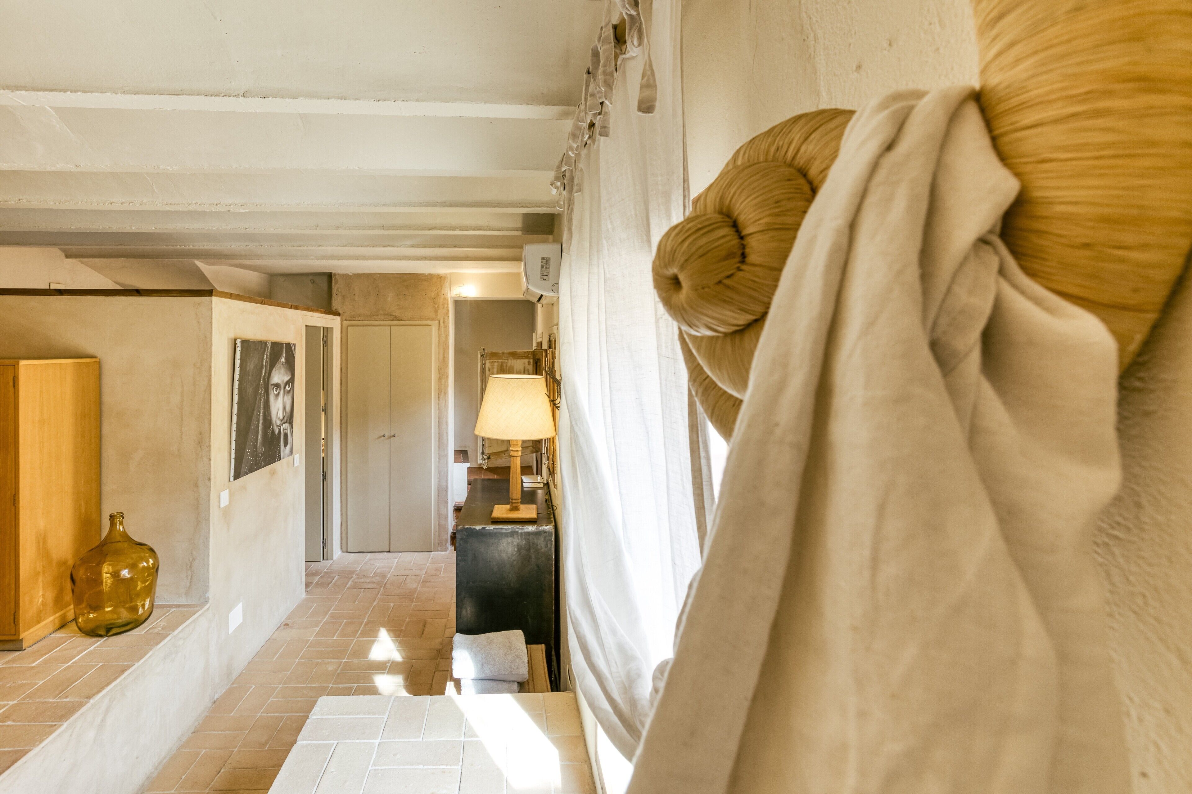 A hallway with a tiled floor, a wooden cabinet, a lamp, and a door in the background.