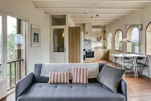 A modern living room with a grey sofa, striped cushions, a dining area with a table and chairs, and a kitchen in the background. - Apartment 'El Pedró Rural' with Mountain View, Wi-Fi and Air Conditioning (Ventalló)