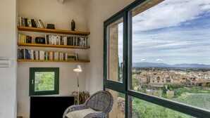 Una habitación con un gran ventanal, una silla de mimbre, una estantería y una lámpara.